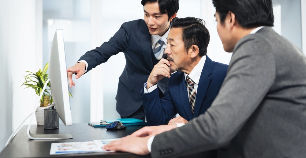 3人の面接官がPCの画面で応募者の提出物を見ながら評価を相談している様子